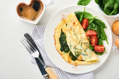 Ispanaklı omlet, kiraz domatesli ve biberli omlet beyaz tabakta, açık gri arkaplanda. Sağlıklı kahvaltı konsepti. Üst görünüm.