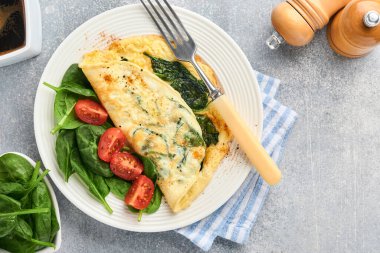 Ispanaklı omlet, kiraz domatesli ve biberli omlet beyaz tabakta, açık gri arkaplanda. Sağlıklı kahvaltı konsepti. Üst görünüm.