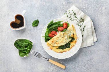 Ispanaklı omlet, kiraz domatesli ve biberli omlet beyaz tabakta, açık gri arkaplanda. Sağlıklı kahvaltı konsepti. Üst görünüm.