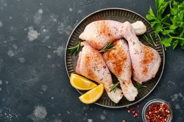 Siyah taştan bir arka planda pişirmek için malzemeli çiğ tavuk budu. Yiyecek arka planı, siyah masada baharatlı çiğ et. Üst görünüm.
