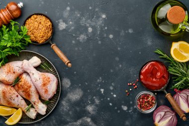 Siyah taştan bir arka planda pişirmek için malzemeli çiğ tavuk budu. Yiyecek arka planı, siyah masada baharatlı çiğ et. Üst görünüm.