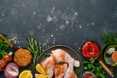 Siyah taştan bir arka planda pişirmek için malzemeli çiğ tavuk budu. Yiyecek arka planı, siyah masada baharatlı çiğ et. Üst görünüm.
