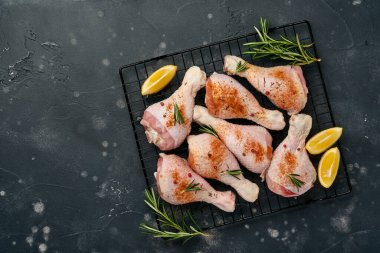 Siyah taştan bir arka planda pişirmek için malzemeli çiğ tavuk budu. Yiyecek arka planı, siyah masada baharatlı çiğ et. Üst görünüm.
