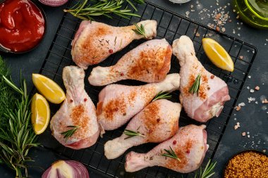 Siyah taştan bir arka planda pişirmek için malzemeli çiğ tavuk budu. Yiyecek arka planı, siyah masada baharatlı çiğ et. Üst görünüm.