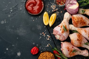 Siyah taştan bir arka planda pişirmek için malzemeli çiğ tavuk budu. Yiyecek arka planı, siyah masada baharatlı çiğ et. Üst görünüm.