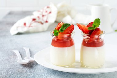 Vanilyalı panna cotta ve taze çilek, gri beton masa arkasında nane yaprakları. Böğürtlenli tatlı. Seçici odak.