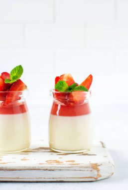 Vanilyalı panna cotta ve taze çilek, gri beton masa arkasında nane yaprakları. Böğürtlenli tatlı. Seçici odak.