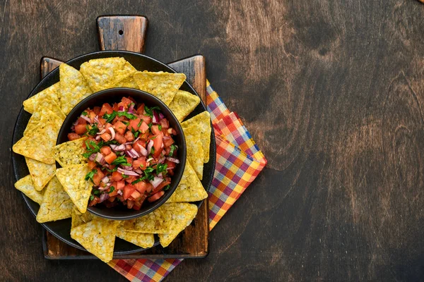 Traditional Mexican tomato sauce salsa with nachos and ingredients tomatoes, chile, garlic, onion on dark old wooden background. Concept of Latin American and Mexican food. Mock up.