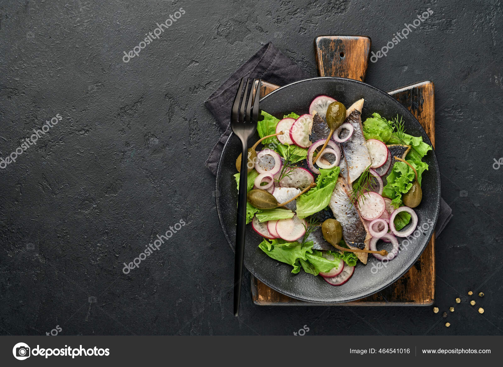 Salted herring with spice, capers, herbs and onion salad on black plate