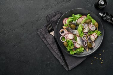 Baharatlı tuzlanmış ringa balığı, kapari, otlar ve siyah tabakta soğan salatası fotokopi alanı ile birlikte siyah arka planda. Salamura edilmiş balık. Sağlıklı doymamış yağlı yiyecekler.