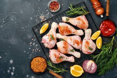 Siyah taştan bir arka planda pişirmek için malzemeli çiğ tavuk budu. Yiyecek arka planı, siyah masada baharatlı çiğ et. Üst görünüm.
