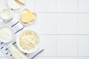Beyaz masa arkasında bir bardak süt, süzme peynir, ricotta, ekşi krema, peynir, camembert ve tereyağı. Farklı süt ürünleri. Süt konsepti. Kopyalama alanı olan üst görünüm. Model.