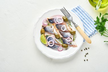 Baharatlı tuzlu ringa balığı, otlar ve soğan beyaz tabakta, ışık taşından arka planda fotokopi alanı ile birlikte. Salamura edilmiş balık. Sağlıklı doymamış yağlı yiyecekler.