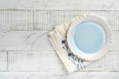 Tarifiniz veya menünüz için eski beyaz tahta masa arkaplanının üzerine boş beyaz tabak ve mavi havlu koyun. Üst Manzara. Model.