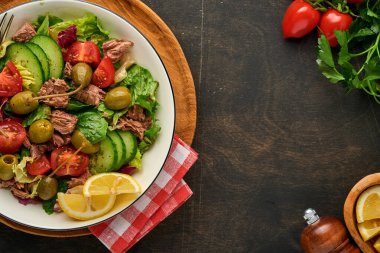 Taze sebzeli, zeytinli, kapari ve limonlu ton balığı salatası eski ahşap arka planda servis edilir. Kopyalama alanı olan üst görünüm.