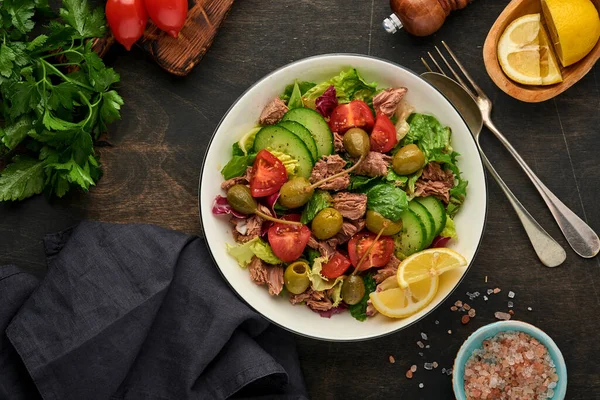 Taze sebzeli, zeytinli, kapari ve limonlu ton balığı salatası eski ahşap arka planda servis edilir. Kopyalama alanı olan üst görünüm.
