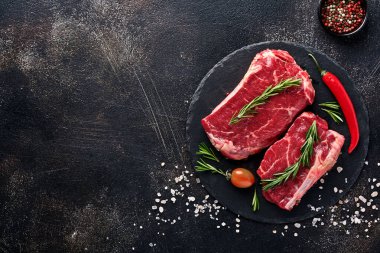 New York usulü iki çiğ biftek, biberiye ve baharatlı parşömen kağıdının üzerinde eski, siyah taştan bir arka plan. Üst Manzara. Model.