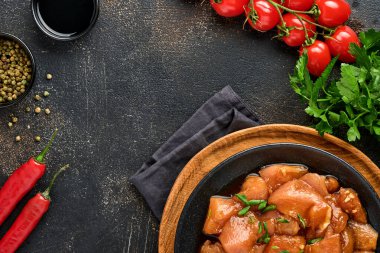 Teriyaki soya sosunda marine edilmiş çiğ tavuk eti, soğan ve biber siyah bir tabakta, taş, beton arka planda. Kopyalama alanı olan üst görünüm.