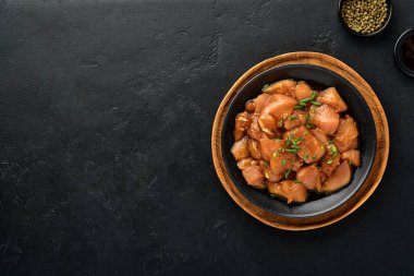 Teriyaki soya sosunda marine edilmiş çiğ tavuk eti, soğan ve biber siyah bir tabakta, taş, beton arka planda. Kopyalama alanı olan üst görünüm.