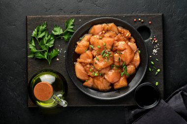 Teriyaki soya sosunda marine edilmiş çiğ tavuk eti, soğan ve biber siyah bir tabakta, taş, beton arka planda. Kopyalama alanı olan üst görünüm.