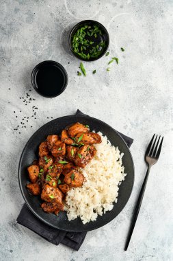 Baharatlı teriyaki tavuğu pirinçli fileto, yeşil soğanlı ve siyah susam tohumlu gri levha, taş ya da beton zemin üzerinde. Kopyalama alanı olan üst görünüm.