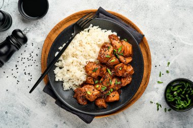 Baharatlı teriyaki tavuğu pirinçli fileto, yeşil soğanlı ve siyah susam tohumlu gri levha, taş ya da beton zemin üzerinde. Kopyalama alanı olan üst görünüm.