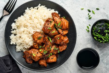Baharatlı teriyaki tavuğu pirinçli fileto, yeşil soğanlı ve siyah susam tohumlu gri levha, taş ya da beton zemin üzerinde. Kopyalama alanı olan üst görünüm.