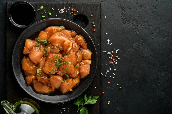 Teriyaki soya sosunda marine edilmiş çiğ tavuk eti, soğan ve biber siyah bir tabakta, taş, beton arka planda. Kopyalama alanı olan üst görünüm.