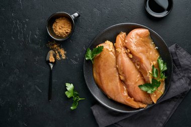 Teriyaki soya sosunda marine edilmiş çiğ tavuk filetosu, soğan, sarımsak ve biber siyah tabakta, taş ya da beton zeminde. Kopyalama alanı olan üst görünüm.