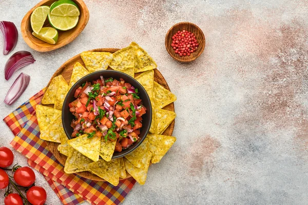 Traditional Mexican tomato sauce salsa with nachos and ingredients tomatoes, chile, garlic, onion on light slate stone background. Concept of Latin American and Mexican food. Mock up.