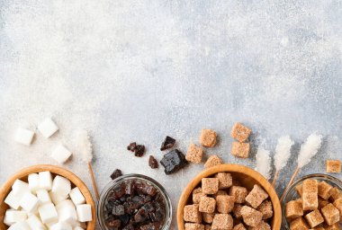 Beyaz şeker, kamış şekeri küpleri, gri masa zemininde bambu kasesinde karamel. Farklı şeker çeşitleri vardı. Üst görünüm veya düz uzanma.