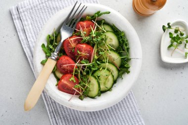 Domatesli taze salata, salatalık, sebze, gri taş zemin üzerinde beyaz tabakta mikroyeşil turplar. Yukarıdan bak. Vejetaryen ve sağlıklı beslenmeyi düşün..