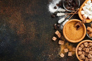 Beyaz şeker, kamış şeker küpleri, koyu kahverengi masa çimento zemininde bambu kasesinde karamel. Farklı şeker çeşitleri vardı. Üst görünüm veya düz uzanma.