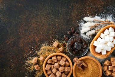 Beyaz şeker, kamış şeker küpleri, koyu kahverengi masa çimento zemininde bambu kasesinde karamel. Farklı şeker çeşitleri vardı. Üst görünüm veya düz uzanma.