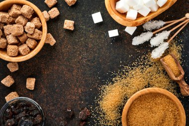 Beyaz şeker, kamış şeker küpleri, koyu kahverengi masa çimento zemininde bambu kasesinde karamel. Farklı şeker çeşitleri vardı. Üst görünüm veya düz uzanma.