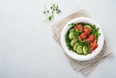 Domatesli taze salata, salatalık, sebze, gri taş zemin üzerinde beyaz tabakta mikroyeşil turplar. Yukarıdan bak. Vejetaryen ve sağlıklı beslenmeyi düşün..