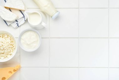 Beyaz masa arkasında bir bardak süt, süzme peynir, ricotta, ekşi krema, peynir, camembert ve tereyağı. Farklı süt ürünleri. Süt konsepti. Kopyalama alanı olan üst görünüm. Model.