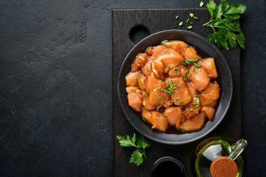 Teriyaki soya sosunda marine edilmiş çiğ tavuk eti, soğan ve biber siyah bir tabakta, taş, beton arka planda. Kopyalama alanı olan üst görünüm.