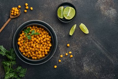 Kızarmış nohut, maydanozlu zerdeçal ve siyah tabakta limon, eski bir siyah masa arkasında. Kızarmış baharatlı nohut ya da Hint chana 'sı ya da kolesistektomi, popüler atıştırma tarifi. Üst görünüm.