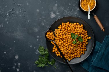 Kızarmış nohut, maydanozlu zerdeçal ve siyah tabakta limon, eski bir siyah masa arkasında. Kızarmış baharatlı nohut ya da Hint chana 'sı ya da kolesistektomi, popüler atıştırma tarifi. Üst görünüm.