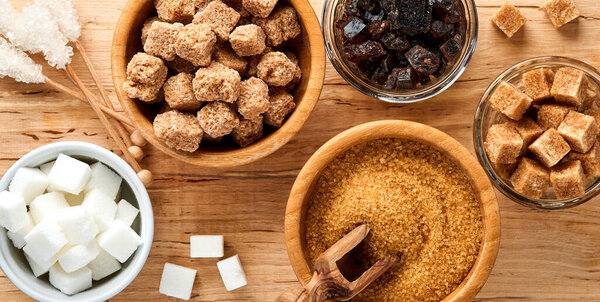 White sugar, cane sugar cubes, caramel in bamboo bowl on dark brown table concrete background. Assorted different types of sugar. Top view or flat lay.