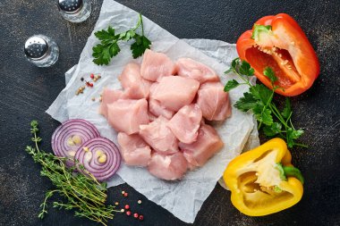 Tahtadaki tavuğun çiğ parçaları, baharatlar, otlar ve sebzeler koyu gri arka planda. Gulaş ya da şiş kebap için ham malzeme. Üst Manzara. Boş kopyalama alanı.