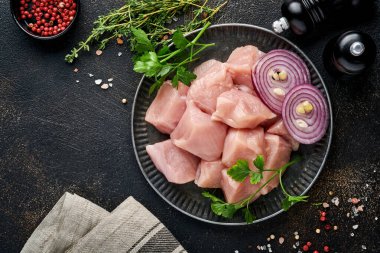 Tahtadaki tavuğun çiğ parçaları, baharatlar, otlar ve sebzeler koyu gri arka planda. Gulaş ya da şiş kebap için ham malzeme. Üst Manzara. Boş kopyalama alanı.