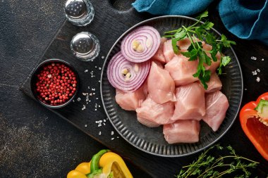 Tahtadaki tavuğun çiğ parçaları, baharatlar, otlar ve sebzeler koyu gri arka planda. Gulaş ya da şiş kebap için ham malzeme. Üst Manzara. Boş kopyalama alanı.