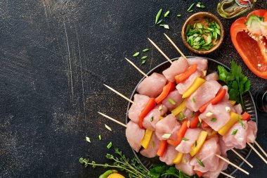 Ahşap tahtada çiğ şiş kebap, baharatlar, otlar ve koyu gri arka planda sebzeler. Gulaş ya da şiş kebap için mangal malzemesi. Üst Manzara. Boş kopyalama alanı.