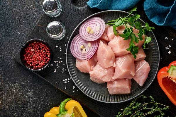 Tahtadaki tavuğun çiğ parçaları, baharatlar, otlar ve sebzeler koyu gri arka planda. Gulaş ya da şiş kebap için ham malzeme. Üst Manzara. Boş kopyalama alanı.