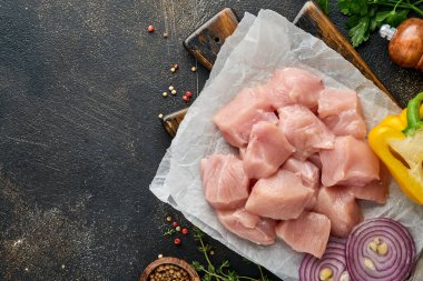 Tahtadaki tavuğun çiğ parçaları, baharatlar, otlar ve sebzeler koyu gri arka planda. Gulaş ya da şiş kebap için ham malzeme. Üst Manzara. Boş kopyalama alanı.
