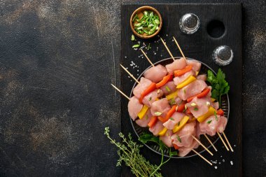 Ahşap tahtada çiğ şiş kebap, baharatlar, otlar ve koyu gri arka planda sebzeler. Gulaş ya da şiş kebap için mangal malzemesi. Üst Manzara. Boş kopyalama alanı.