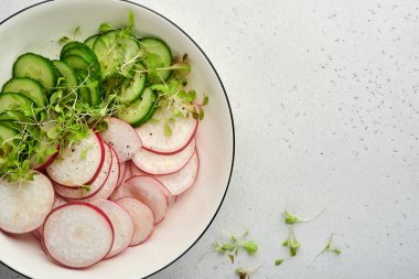 Kırmızı turplu taze salata, salatalık, sebzeler, gri taş zemin üzerinde beyaz tabakta mikroyeşil turplar. Yukarıdan bak. Vejetaryen ve sağlıklı beslenmeyi düşün..