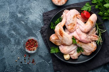 Metal tavada ya da kasede çiğ tavuk kanadı ve koyu gri kayrak, taş ya da beton arka planda yemek pişirmek için baharat ve malzemeler. Siyah masada baharatlı çiğ et. Üst Manzara. Model.